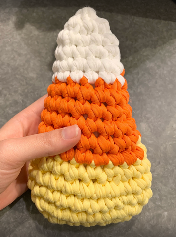 A crocheted candy corn plush on a gray background