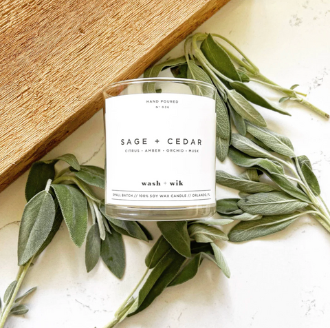 A wash + wik candle, scented sage + cedar, laying on top of a bed of leaves