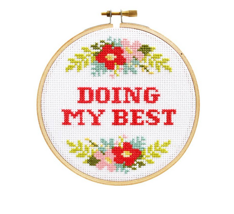 A finished cross-stitch hoop that says "Doing my best" with a floral design bordering it