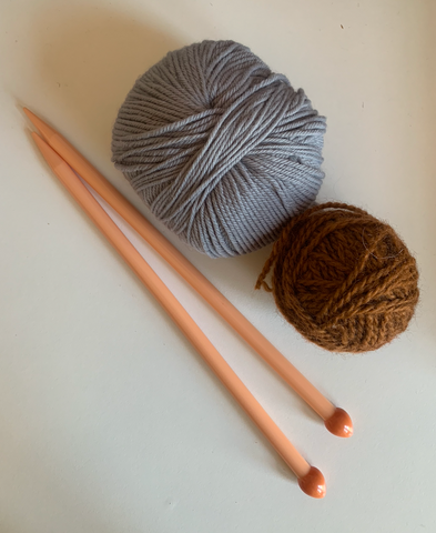 A pair of straight knitting needles laying next to two balls of yarn on a white background.