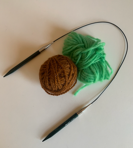 A pair of circular knitting needles laying next to two balls of yarn on a white background.
