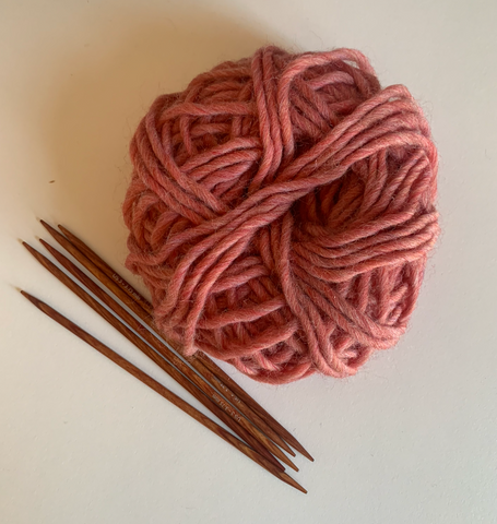 A set of five double pointed knitting needles laying next to a ball of pink yarn on a white background.