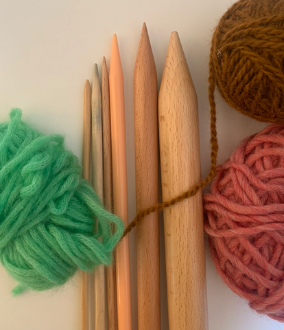 A row of knitting needles from thinnest to thickest, lying next to three balls of yarn.