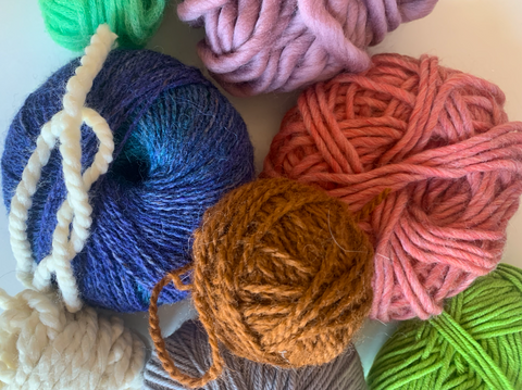 A variety of balls of yarn in different fibers and weights lying on top of each other in a pile.
