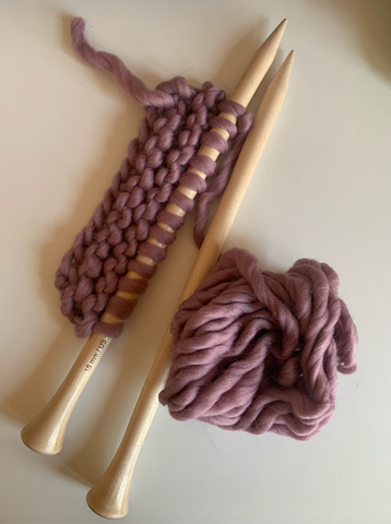 Two knitting needles with the beginning of a purple scarf on one.