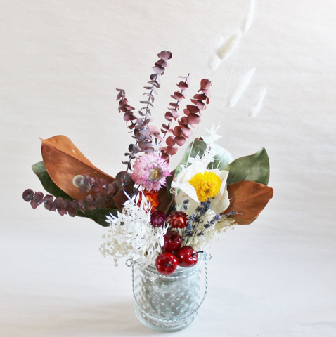 A dried floral arrangement with eucalyptus, magnolia leaves, bunny tails, straw flowers, and lavender in a glass jar
