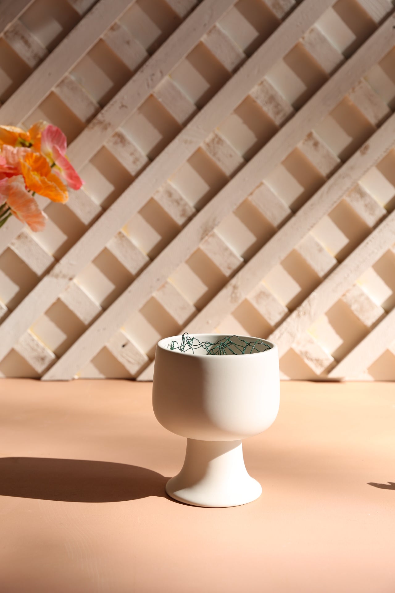 Small white footed bowl on terracotta coloured table with a white textured background