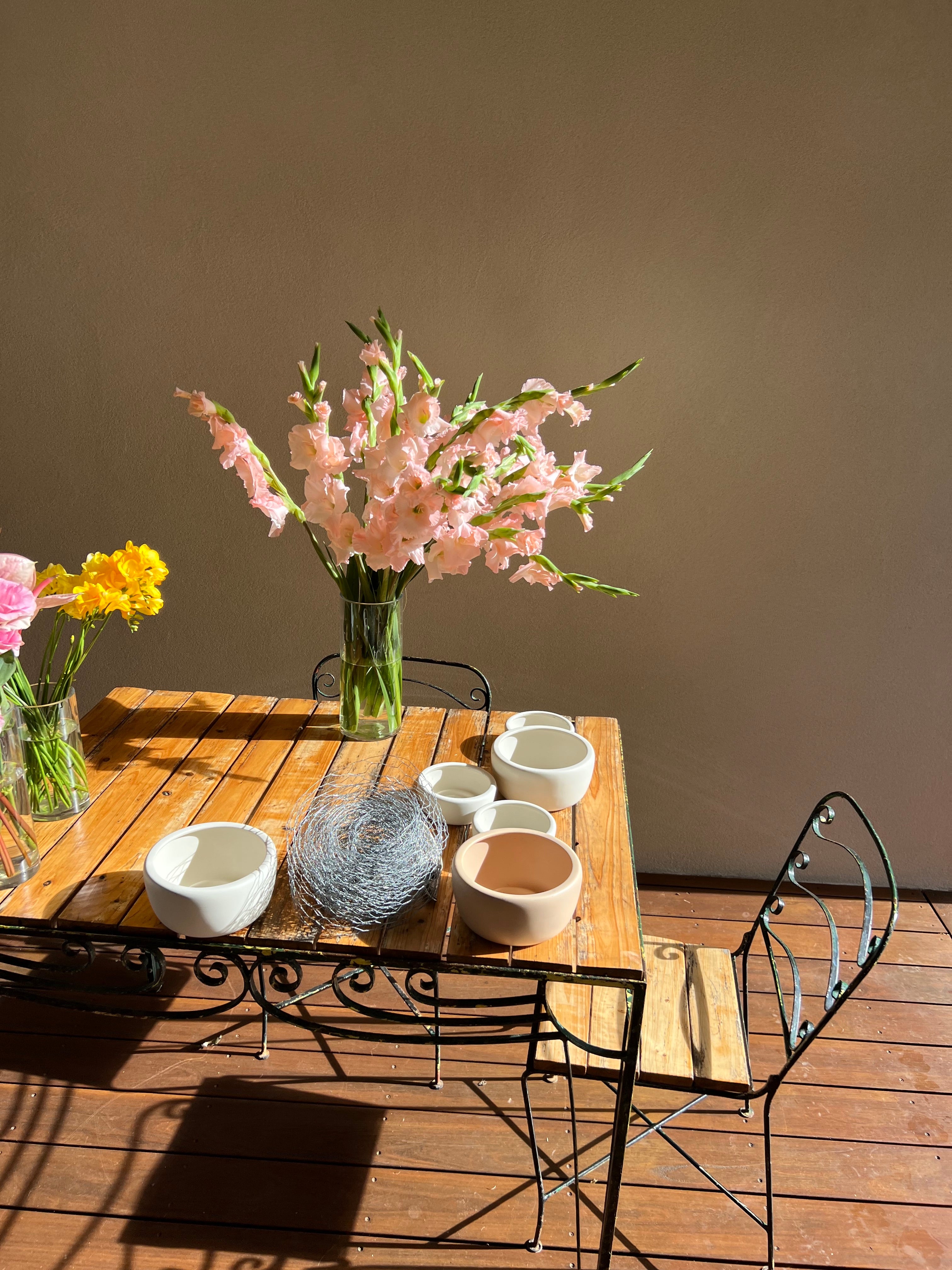 mesa de madera con cuencos de cerámica y un jarrón de flores rosas y rollo de alambre de pollo