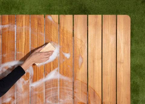 Woman cleaning a teak outdoor table with a soft bristled brush and soap