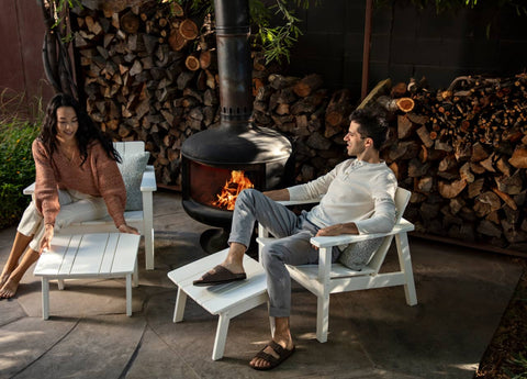Young couple sitting near outdoor fire chiminea and a stack of firewood in background