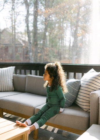 Young girl sitting on outdoor sectional inside a screened porch