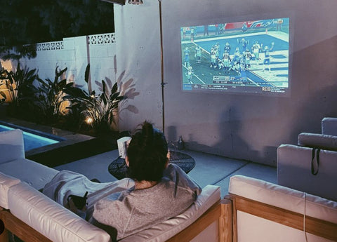 Football game projected on wall at night around an outdoor furniture layout on the porch