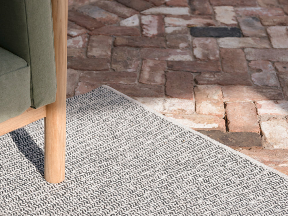 A detail shot of a Neighbor braid rug in pepper nestled beneath a sofa leg