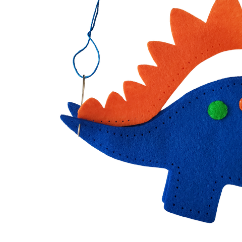 Sewing spikes on blue felt dinosaur