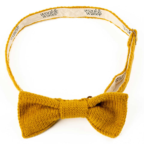 A butterscotch yellow knitted bow tie with it's strap in a circle behind the bow