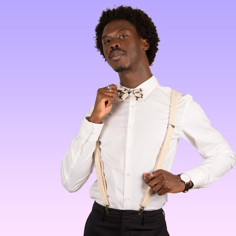 a black man wears a white shirt and cream knitted bow tie with black martini glass motifs and cream knitted suspenders