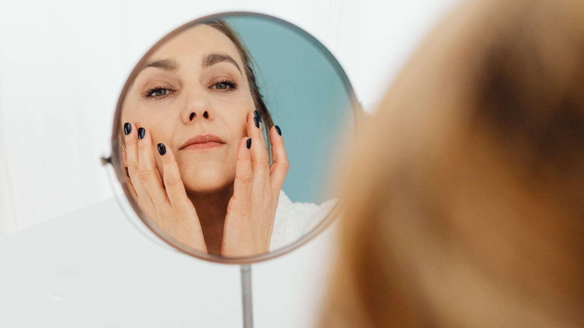 Woman looking at her face in the mirror as she applies skincare products