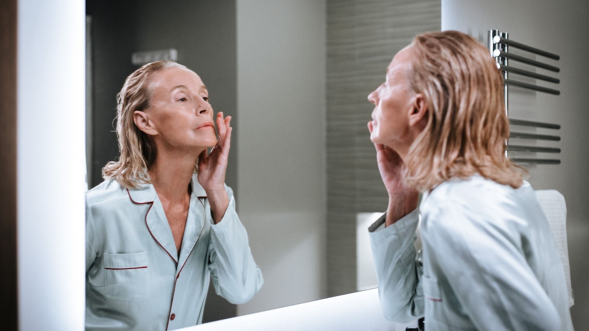 Older woman in pjs in front of the mirror applying face cream