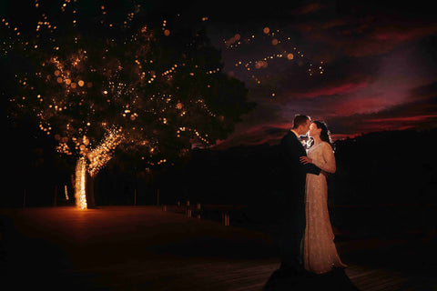 bride and groom kissing in front of a tree at night