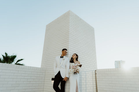 bride and groom posing in front of white brick wall on their wedding day