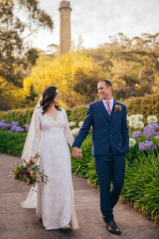 bride and groom walking hand in hand in wedding day attire through gardens