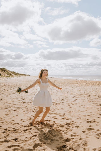 bride dancing in her wedding dress holding flowers on beach