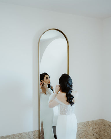 bride fitting into wedding dress in front of mirror and bed