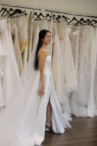 bride in dress walking in front of racks of wedding gowns