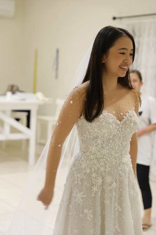 bride in star lace wedding dress holding her veil behind her smiling