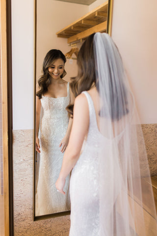 bride looking at her custom wedding gown in the mirror at her hotel