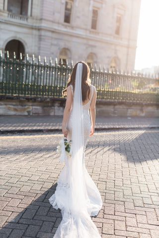 bride walking across brick courtyard in custom gown holding bouquet