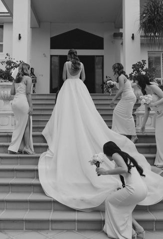 bride walking up stairs while bridesmaids help carry her dress