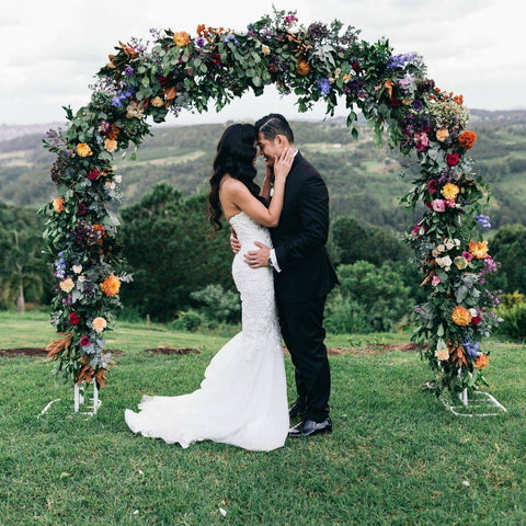 bride wearing wedding dress hugging husband in front of floral arch