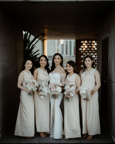 bride wearing wedding dress posing with bridesmaids in their gowns holding bouquets of flowers