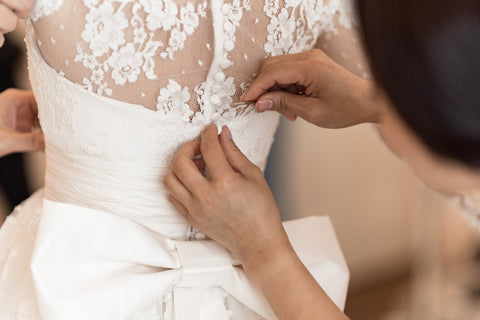 bridesmaid buttoning bride into her custom wedding dress