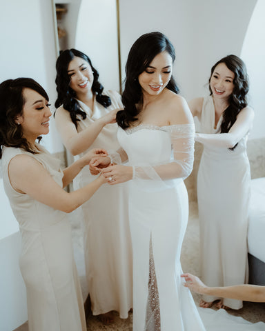 bridesmaids helping bride into her custom wedding dress before her wedding ceremony