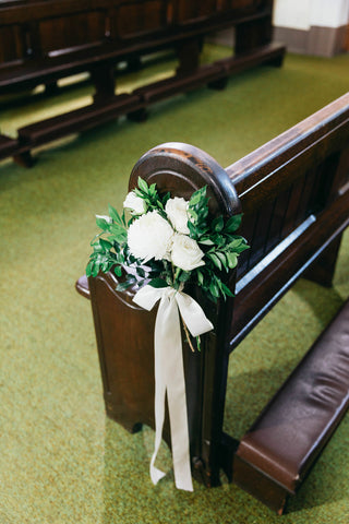 church pew with bridal bouquet hanging from the end