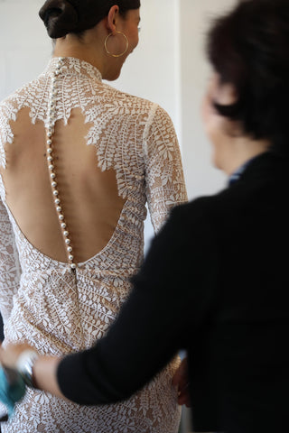 fashion designer helping model into lace wedding dress