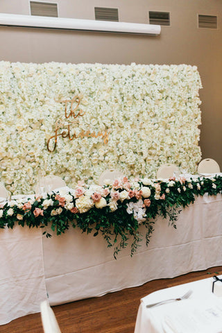 flower wall in front of table with overhanging bouquets