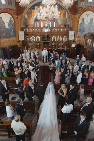 greek church full of guests while bride walks down the aisle