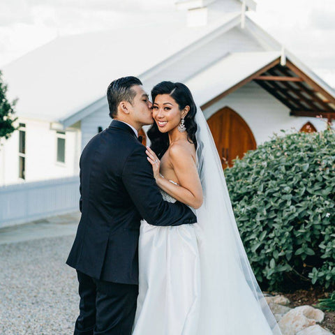 husband kissing wifes cheek in front of church on wedding day