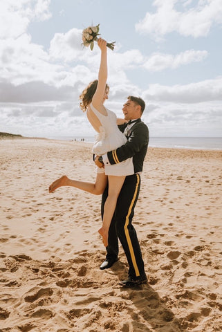 husband lifting up bride on beach