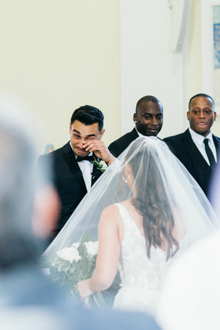 husband wiping tears as he sees his wife for the first time at their wedding day