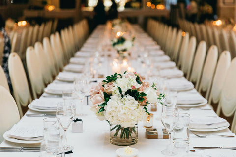 long table at wedding reception with chairs cutlery and bridal bouquets