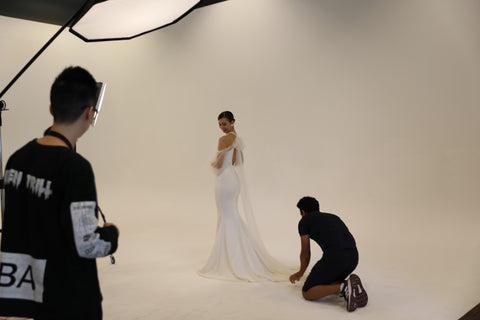 man fixing the train on models wedding dress while videographer films
