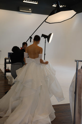 photographer leading model in wedding dress to white room