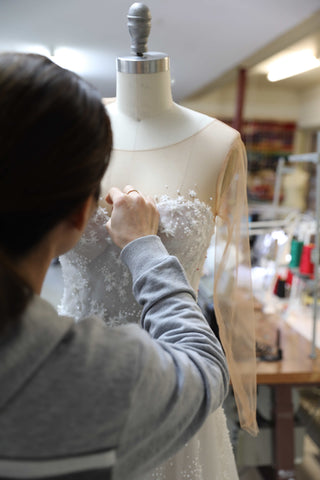 seamstress woman hand sewing star lace onto wedding dress placed on mannequin inside design studio