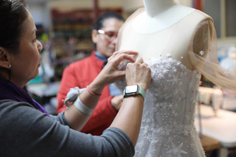two women hand sewing a wedding dress on a mannequin