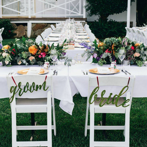 wedding reception seating with bride and groom signs on chairs and flowers with table settings on the tables