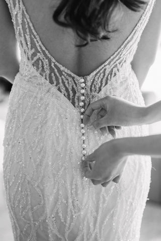 woman buttoning a brides lace wedding dress